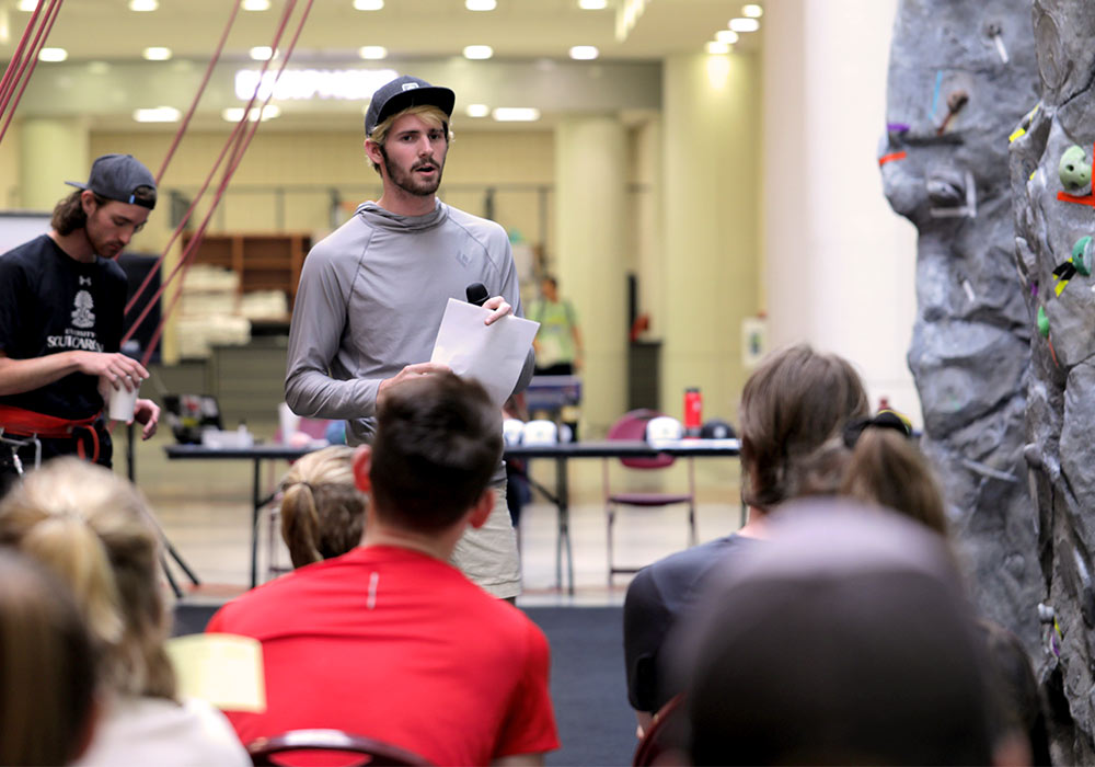 Student worker in Campus Rec stands in front of a group of students giving instructions on using the rock wall.